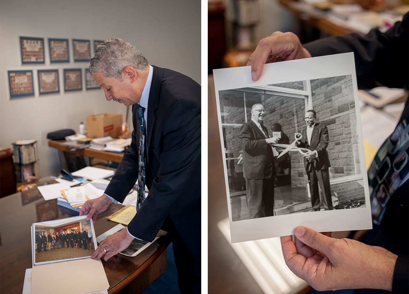 Norman Williams leans over a desk to look throughphotovraphs in a manila folder. He holds up a photograph featuring two mensmiling with a giant pair of scissors.