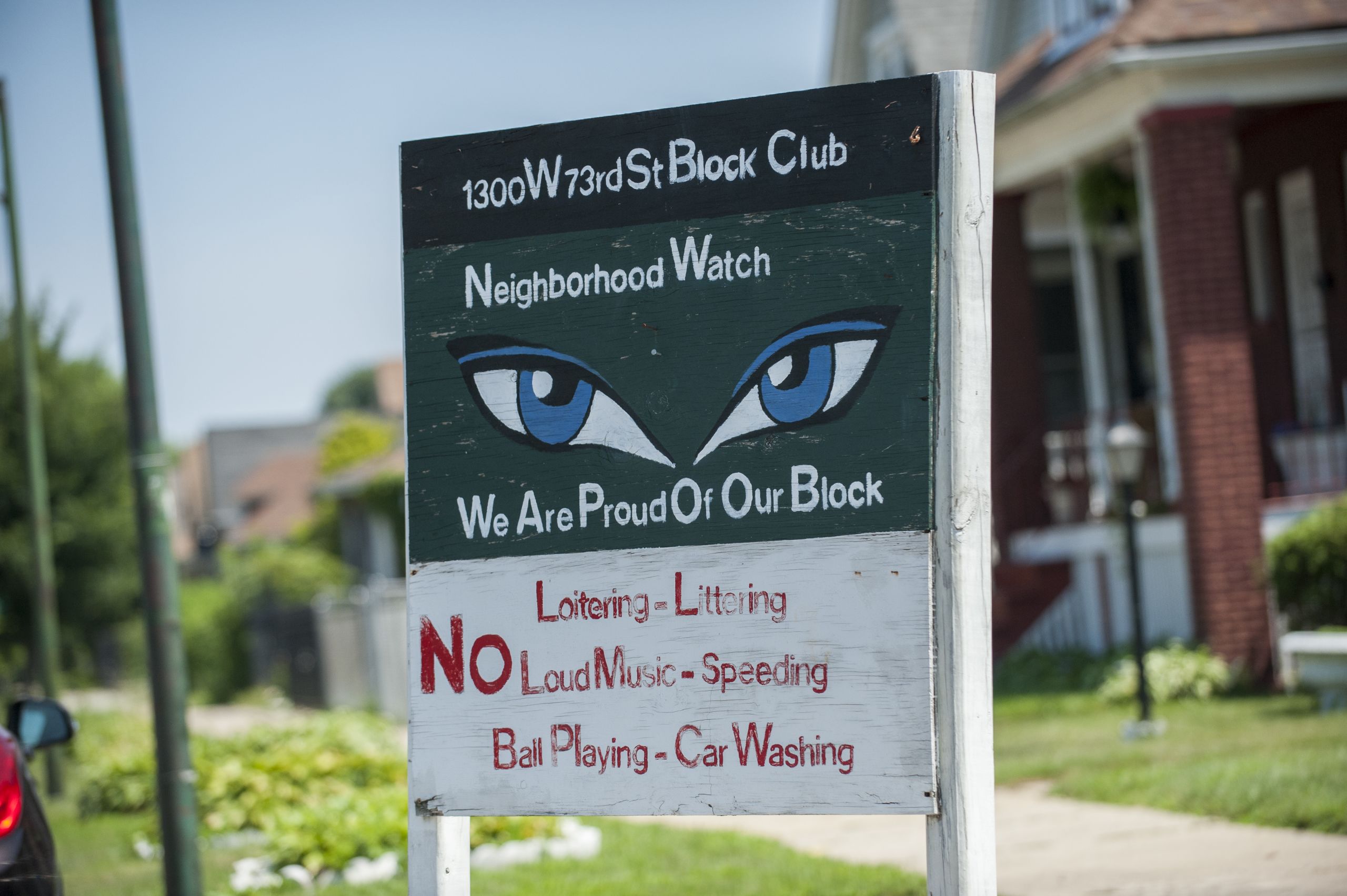 A sign with blue eyes painted on it reads "We Are Proud of Our Block"