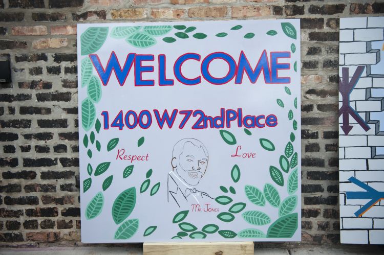 A sign reads "Welcome To 7700 S. Rhodes" in yellow script.