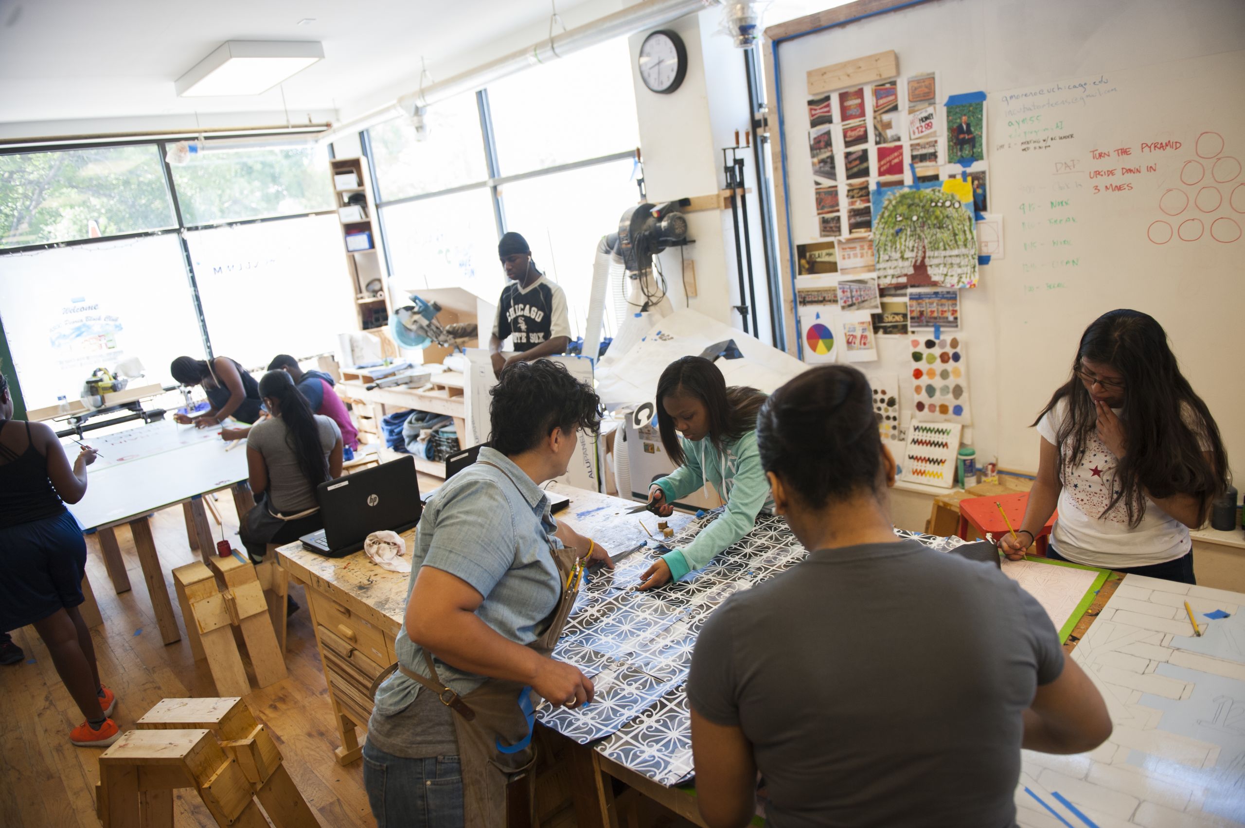 Young people work together in a studio, where art hangs on whiteboards.