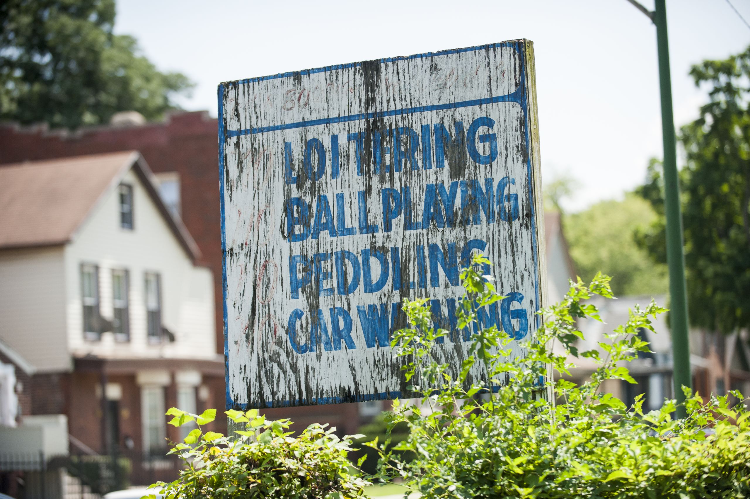 A wooden sign with fading paint reads "Loitering, Ball Playing, Peddling, Car Washing"