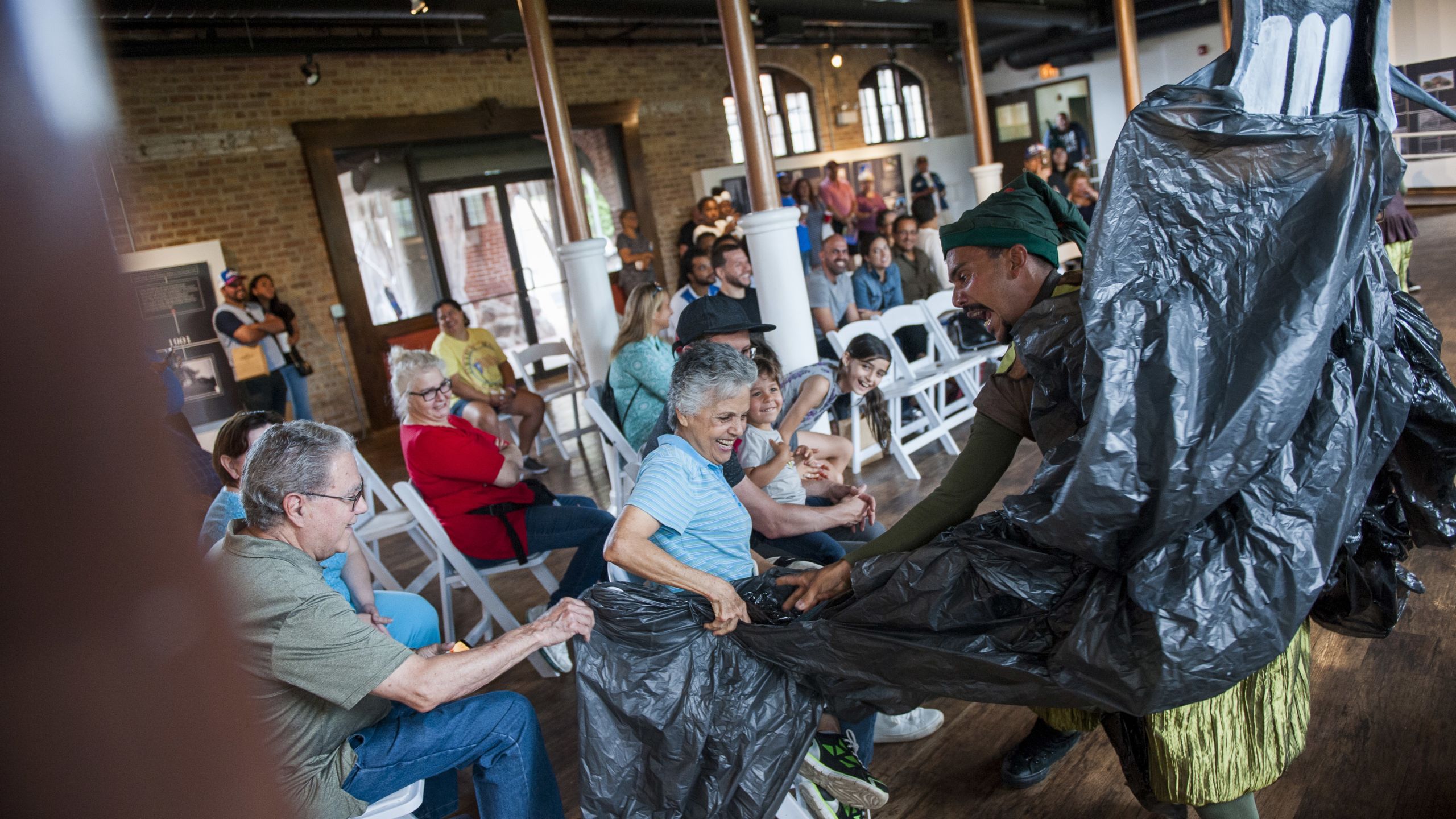 Carlos Jose Torres hands a large trash bag to audience members during a show. The trash bag symbolizes the hurricane.